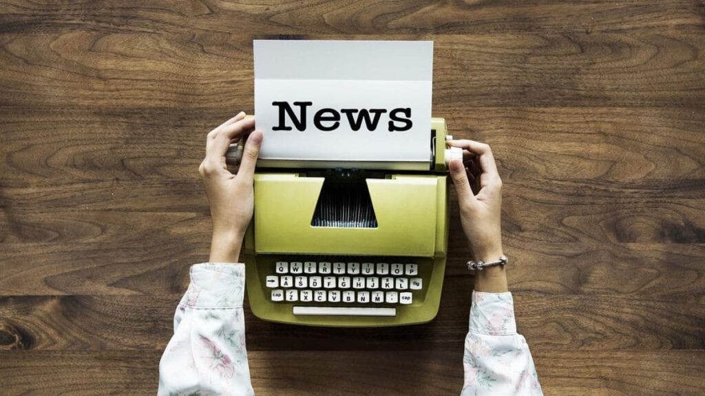 Photo of a person's hands on both sides of a typewriter, from which comes a piece of paper with the word: News.